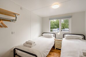 Ein Schlafzimmer mit zwei Betten, einem Fenster mit Blick auf Boote und einer Holzablage.