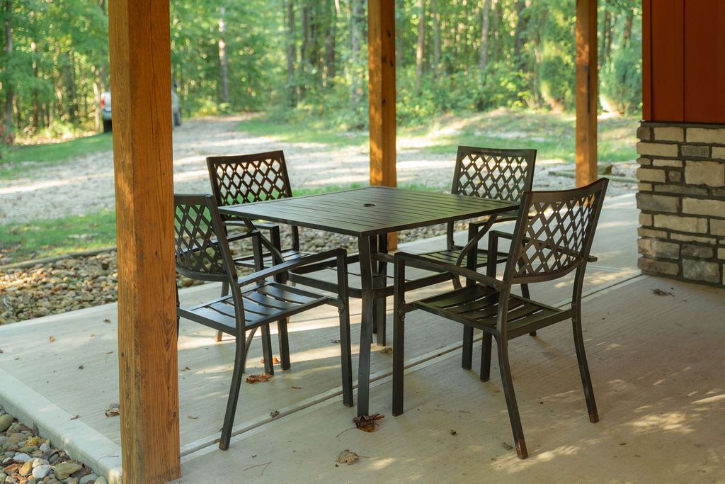 Een terras buiten met een tafel en stoelen, omringd door houten pilaren en een stenen muur.