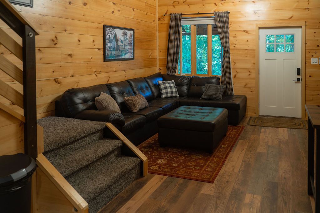 Een houten interieur met een zwarte leren bank, een kamerbreed tapijt met patroon en een trap.
