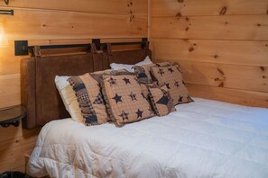 Een kamer met houten lambrisering, een bed, een nachtkastje en een wandlamp.