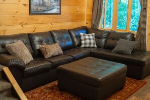 Een zwarte leren modulaire bank met een bijpassend poufje, een ingelijste foto aan de muur en een raam met gordijnen.