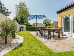 Eine Terrasse mit Tisch und Stühlen, einem blauen Sonnenschirm und einem Kiesweg.