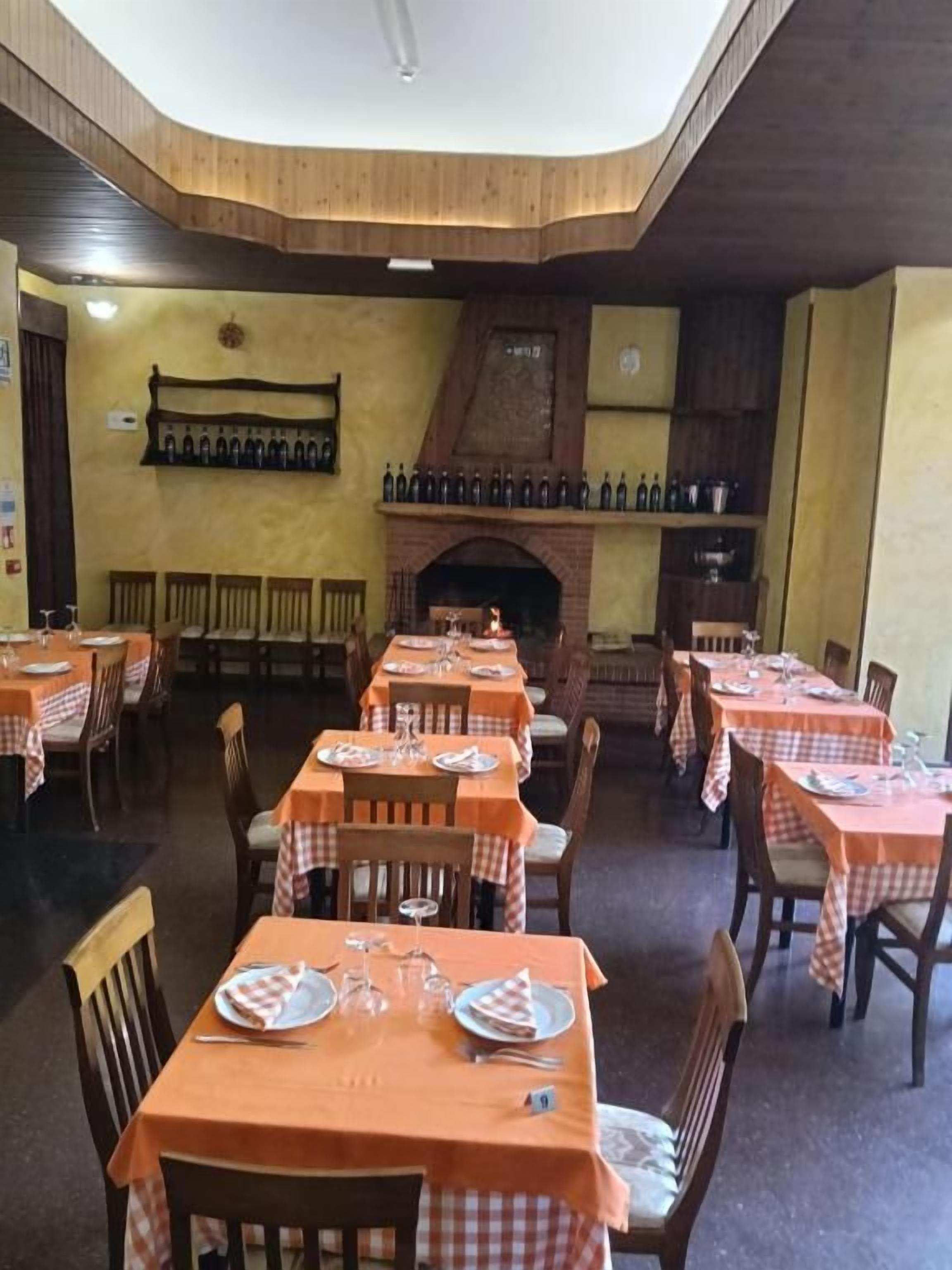Un restaurante con varias mesas dispuestas para comer, una chimenea de ladrillo y una estantería de vinos en la pared.