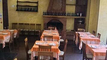 Un restaurante con varias mesas dispuestas para comer, una chimenea de ladrillo y una estantería de vinos en la pared.