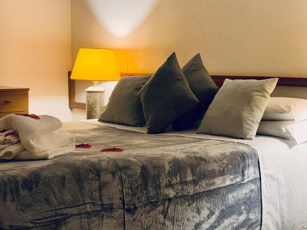 Una cama bien hecha con una colcha gris estampada, una pila de toallas blancas y varias almohadas.