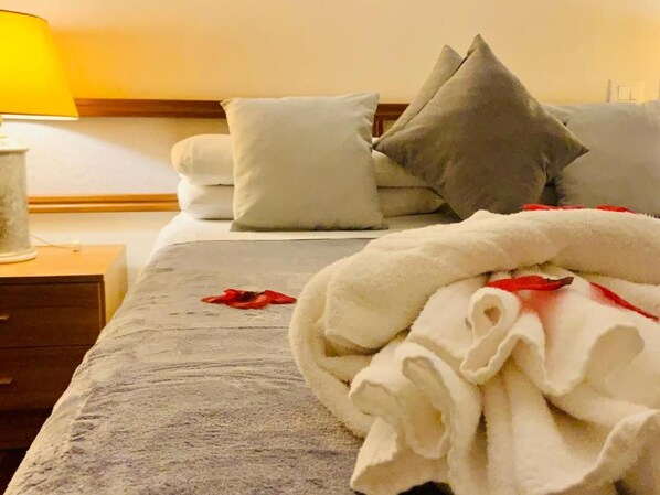 Una habitación de hotel con una cama, almohadas, una mesita de noche y una lámpara.