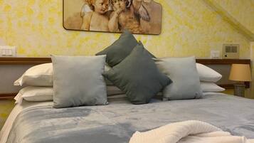 A bedroom with a bed, pillows, a blanket, a wall-mounted artwork, and a nightstand with a lamp.