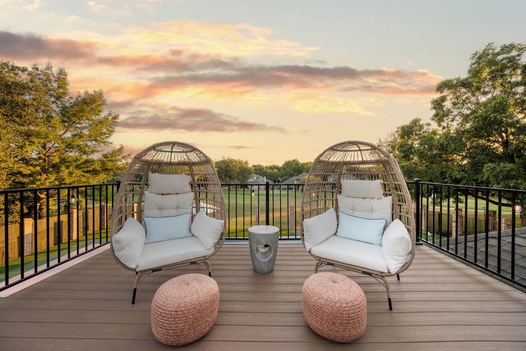 A deck with two wicker chairs and two ottomans, a small table, and a view of a park.