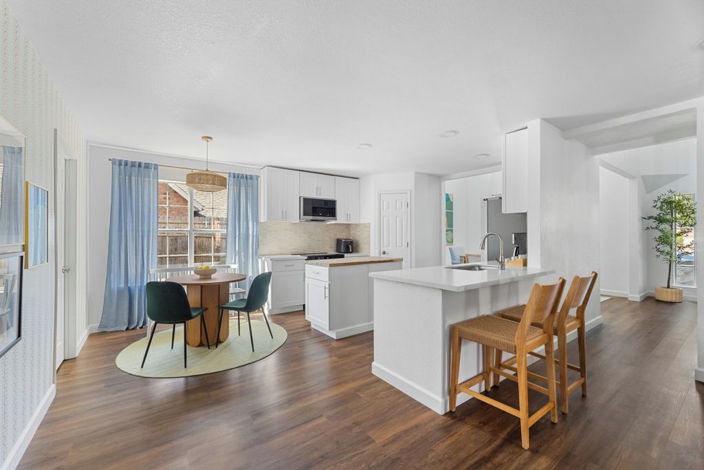 A modern kitchen with white cabinetry, a central island, and a dining area with chairs.