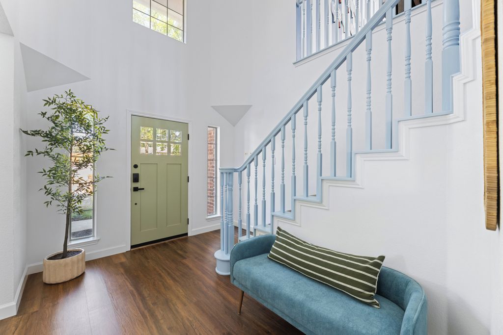 A spacious room with a wooden floor, a blue sofa, a staircase with blue railings, and a green door.