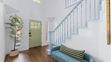 A spacious room with a wooden floor, a blue sofa, a staircase with blue railings, and a green door.