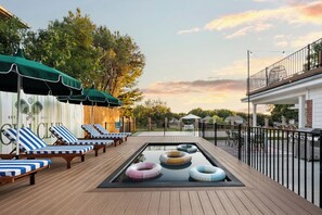 Ein Poolbereich mit Liegestühlen und Sonnenschirmen, umgeben von einer Holzterrasse und einem Zaun.