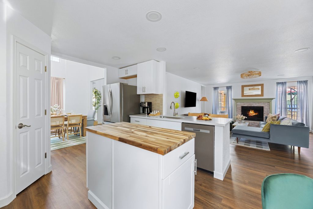 A modern kitchen with white cabinetry, a wooden island, and a dining area with a table and chairs.