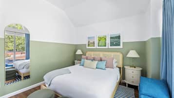 Ein Schlafzimmer mit Bett, Nachttischen, einem Spiegel, einem Fenster und Blick ins Freie.