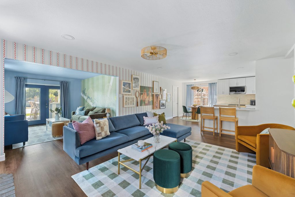 Ein modernes Wohnzimmer mit einem blauen Sofa, einem Couchtisch und einem karierten Teppich. Es gibt eine Küchenzeile mit einem Esstisch und Stühlen.