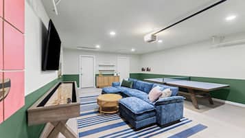 A living room with a blue sofa, a ping pong table, and a billiards table.