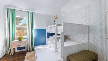 Une chambre avec des lits superposés, une table de chevet, une lampe et une fenêtre avec des rideaux.