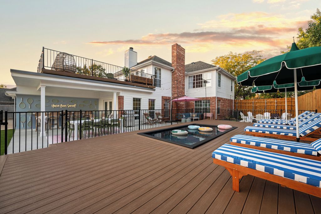 A wooden deck with lounge chairs and a pool table, surrounded by a fence and a building with a sign.
