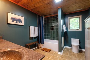 Ein Badezimmer mit einer Badewanne, einer Toilette, einem Waschbecken, einer Duschvorhang und einem Fenster.
