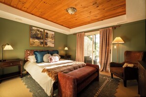 Ein Schlafzimmer mit Holzboden, einem Bett mit vielen Kissen, einer Bank, einem Sessel und zwei Nachttischlampen.