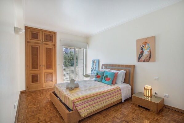 A bedroom with a bed, a nightstand, a painting, and a wooden wardrobe. - Apartment 'Areias Do Mar' (Albufeira)