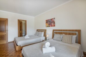 A hotel room with two beds, a painting on the wall, and a wooden door. - Apartment 'Areias Do Mar' (Albufeira)