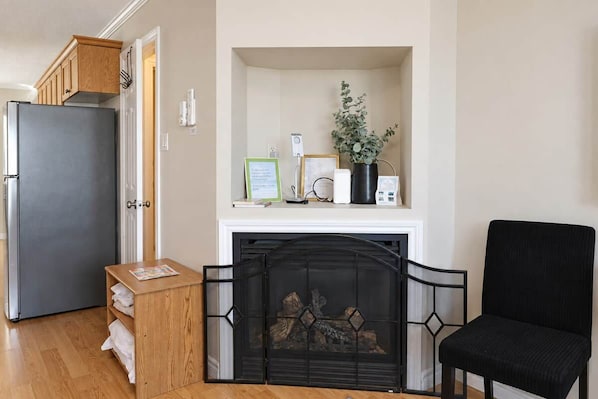 A room with a fireplace, a black chair, a wooden cabinet, and a refrigerator. - Shoreline Retreat-Beach front -Cottage 1 (Wasaga Beach)