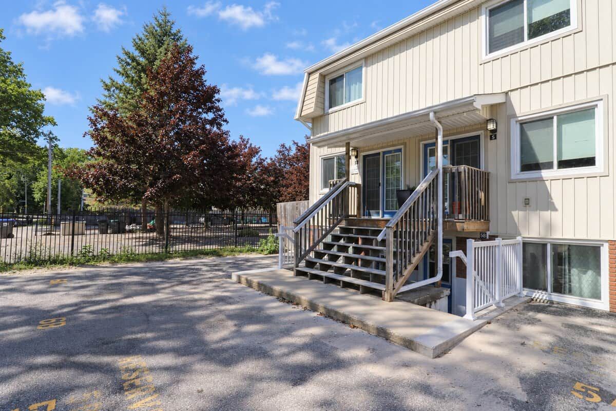 A two-story building with a front entrance, a staircase, and a parking lot with marked spaces.
