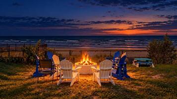 A fire pit with chairs in a grassy area with a view of the ocean at sunset.