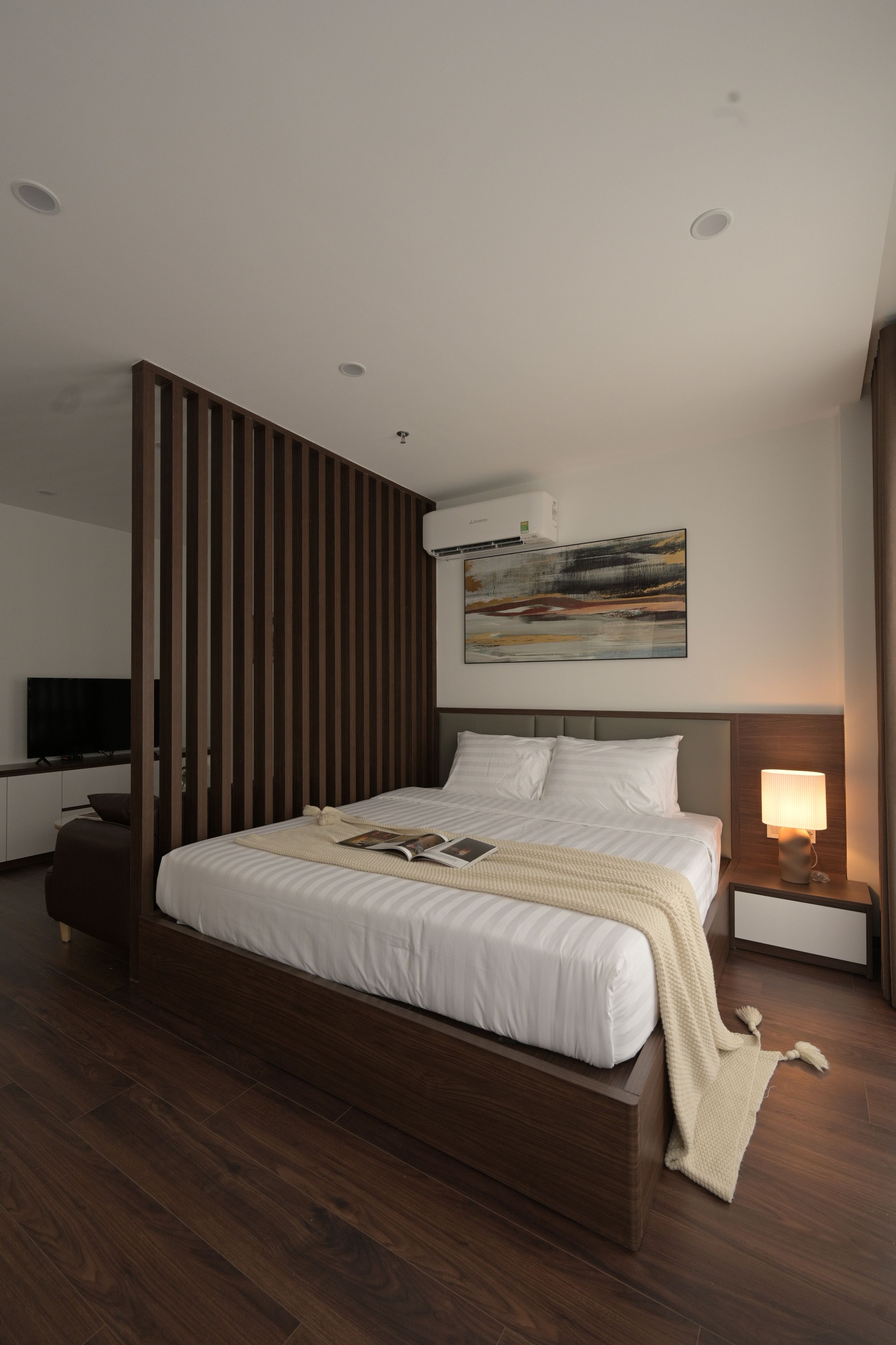 Een moderne hotelkamer met een groot bed, een flatscreen televisie, een nachtkastje met een lamp en een schilderij aan de muur.