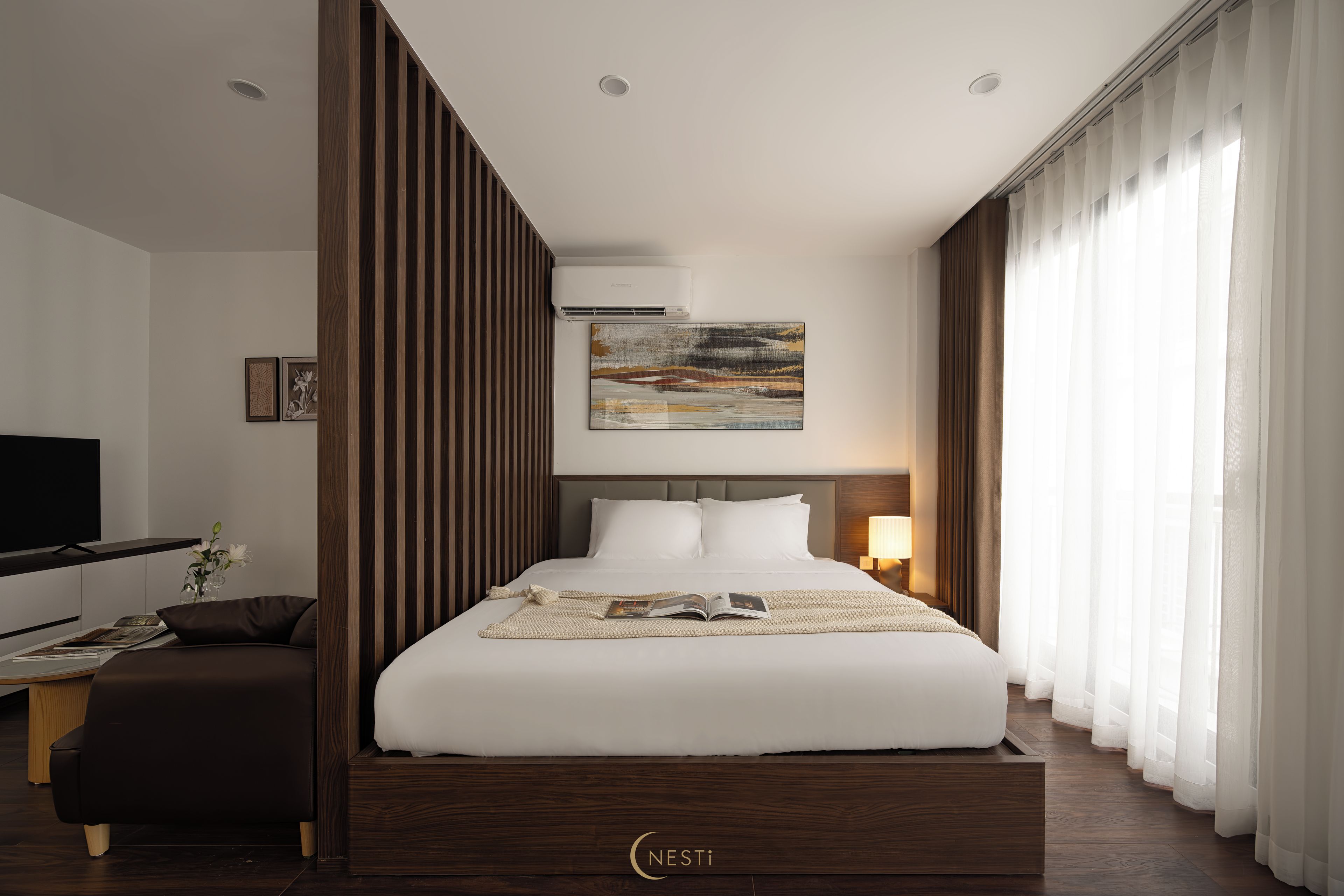 Een moderne hotelkamer met een groot bed, een flatscreen televisie, een bureau met stoel en een raam met dunne gordijnen.