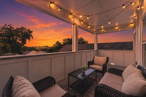 Een overdekt terras met rieten meubilair en lichtjes, met uitzicht op een zonsondergang.