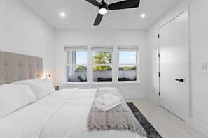 Een slaapkamer met een bed, een plafondventilator, een raam met uitzicht en een deur.