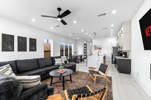 A modern living room with a sofa, coffee table, and chairs, a dining area with a table and chairs, and a kitchen with appliances. - Luxury Texas Home Minutes From Downtown - Sleeps 14 (Dallas)