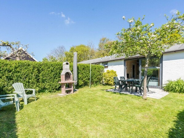 A backyard with a barbecue grill, a covered patio area, and a dining table with chairs. - Holiday Apartment With 2 Bedrooms (Burgh-Haamstede)