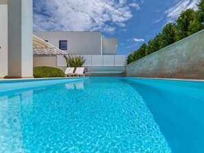 A swimming pool with clear blue water, surrounded by a low wall and a building with a modern design. - Villa in Linardici With Swimming Pool (Krk)