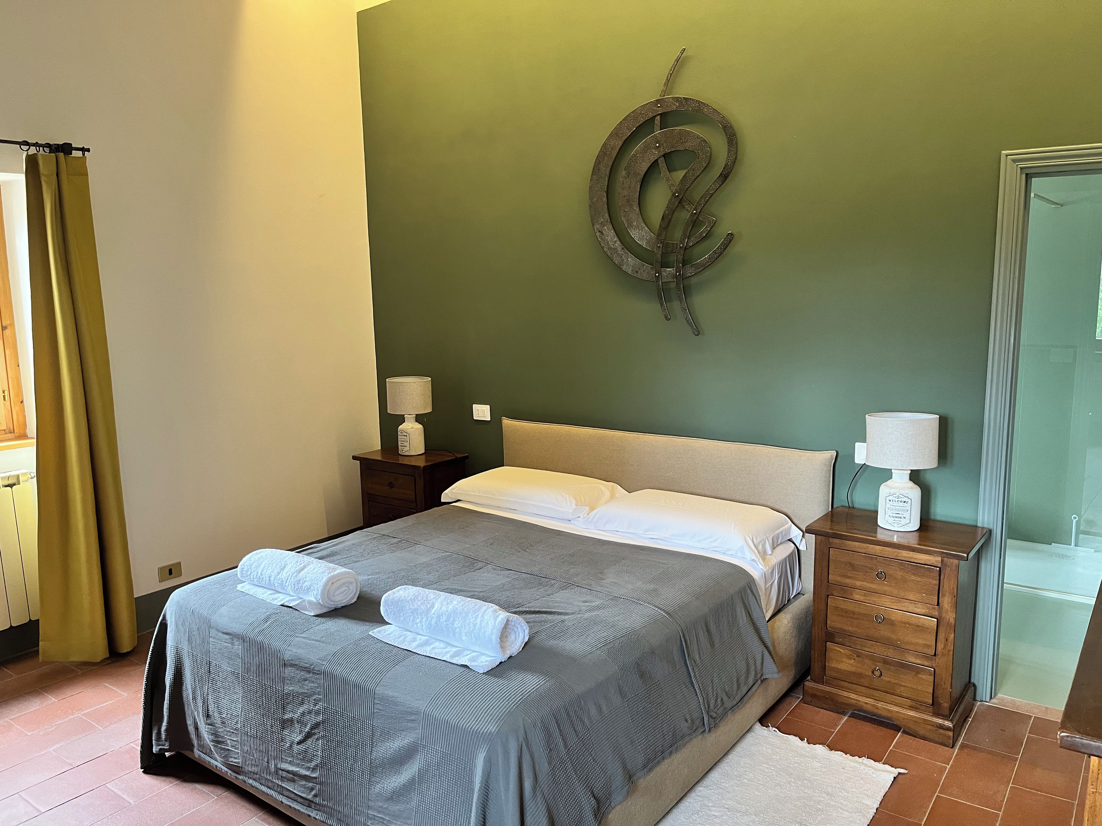 A bedroom with a bed, two bedside tables, a wall-mounted decorative item, and a window with curtains.