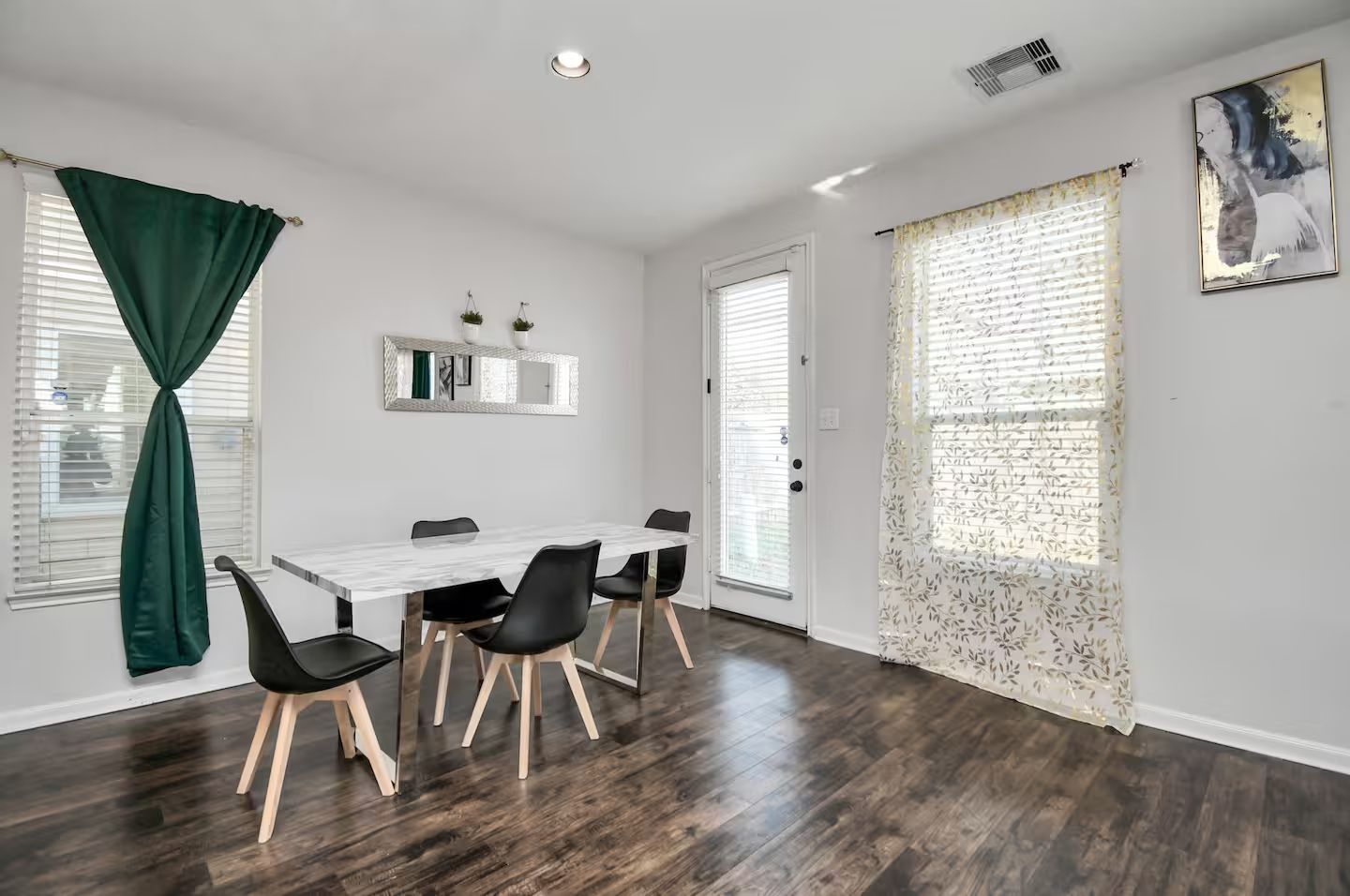 A room with a dining table, chairs, a mirror, and a door with a window.