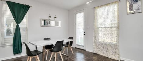 A room with a dining table, chairs, a mirror, and a door with a window.