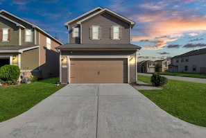 A two-story residential house with a garage, a front lawn, and a clear sky. - Beeline Living (Houston)