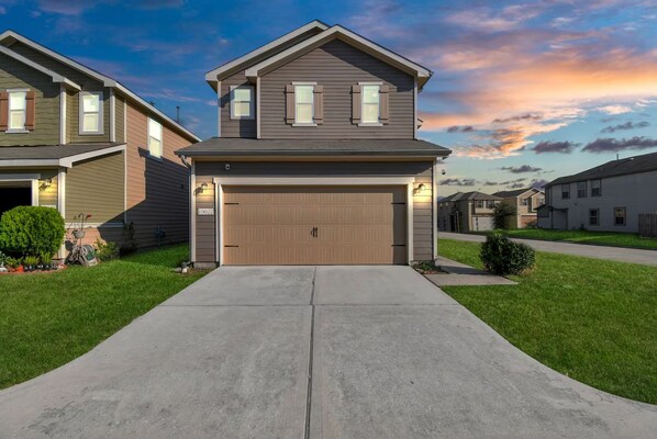 A two-story residential house with a garage, a front lawn, and a clear sky. - Beeline Living (Houston)