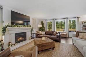 A living room with a fireplace, a large window, and a cozy seating area. - Cozy River Retreat on Deschutes: Hot Tub, Dog Friendly, Game Room + Quality Beds (Three Rivers)