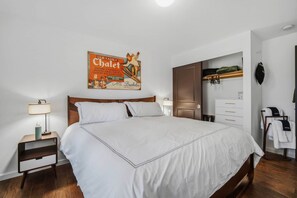 Ein ordentlich eingerichtetes Schlafzimmer mit einem großen Bett, einem Nachttisch mit Lampe, einem Kleiderschrank und einem an der Wand befestigten Haken für Jacken.
