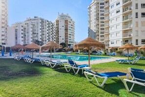 A poolside area with lounge chairs and umbrellas, surrounded by high-rise buildings. - Apartment 'Camões 12 Frente Mar' with Shared Pool and Balcony (Armação de Pêra)