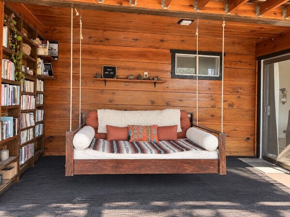 Ein Holzblockhaus-Innenraum mit einer Hängematte, Bücherregalen und einem kleinen Fenster.