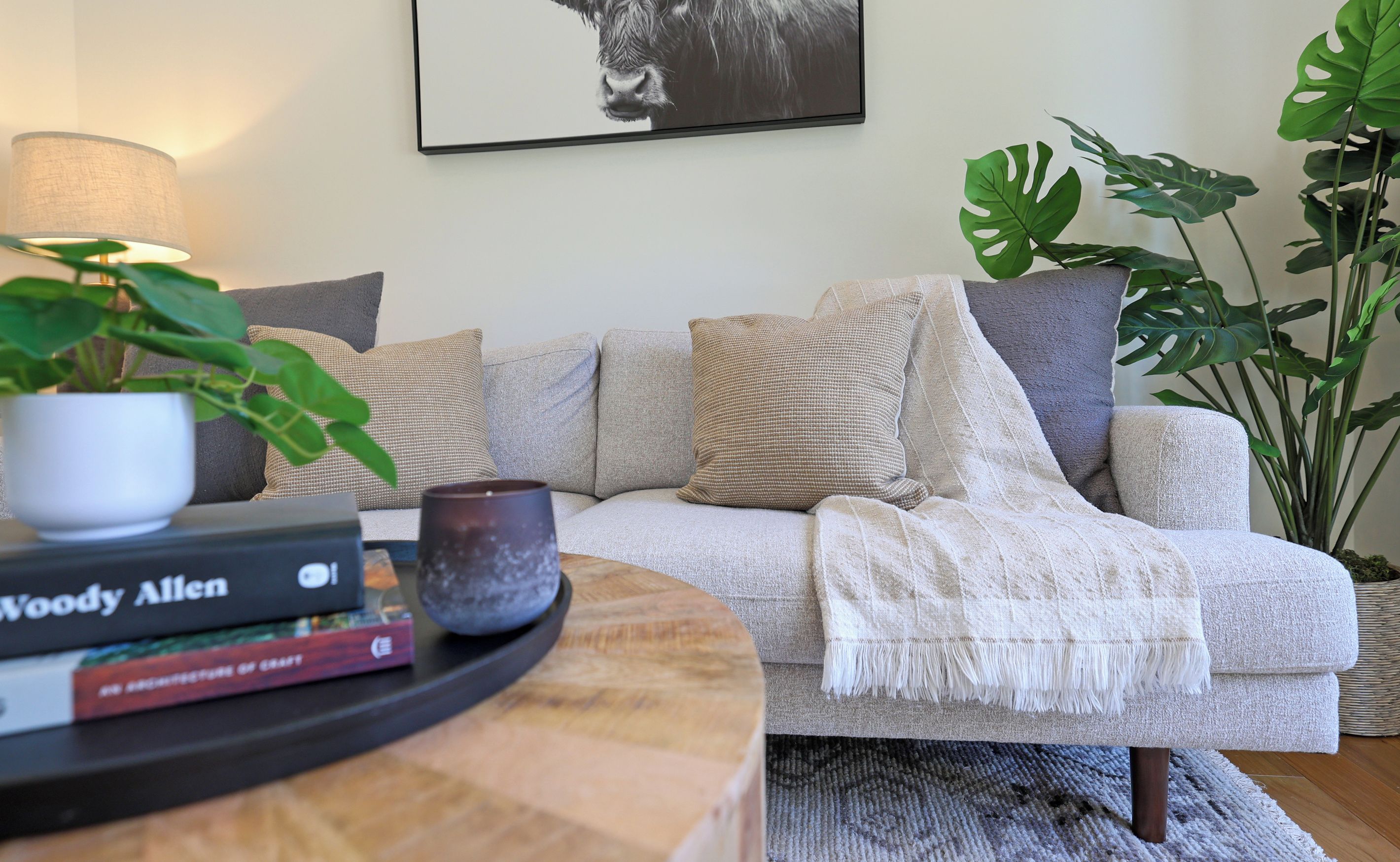 Un salon avec un canapé, une lampe, une plante en pot et un tableau encadré accroché au mur.