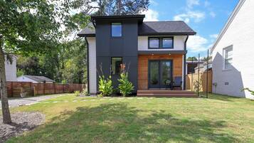A modern two-story house with a dark exterior, a front porch, and a well-maintained lawn.