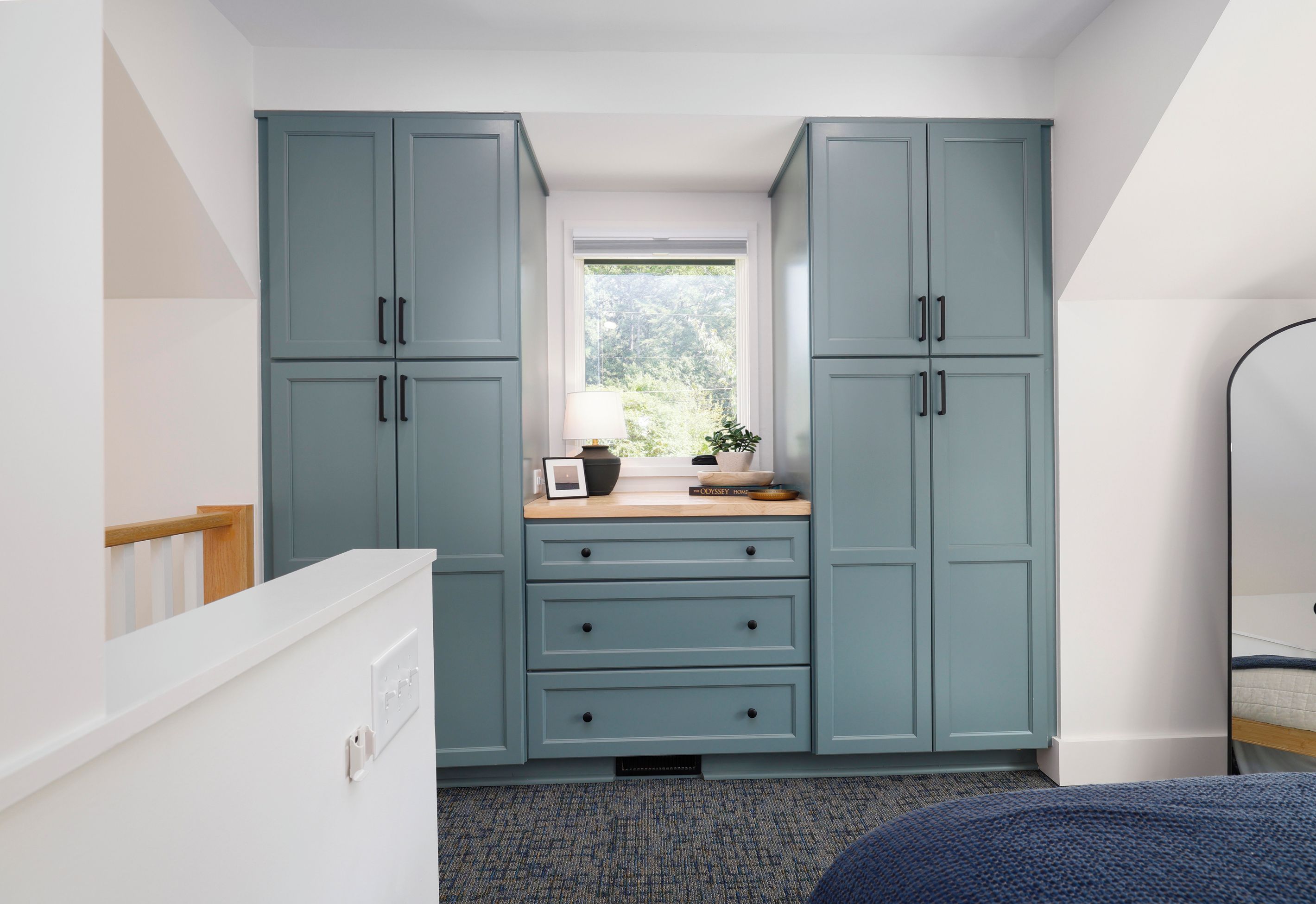 A compact kitchen with teal cabinets, a window with a view of greenery, and a small countertop with a lamp and decorative items.