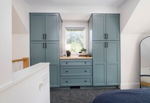 A compact kitchen with teal cabinets, a window with a view of greenery, and a small countertop with a lamp and decorative items.