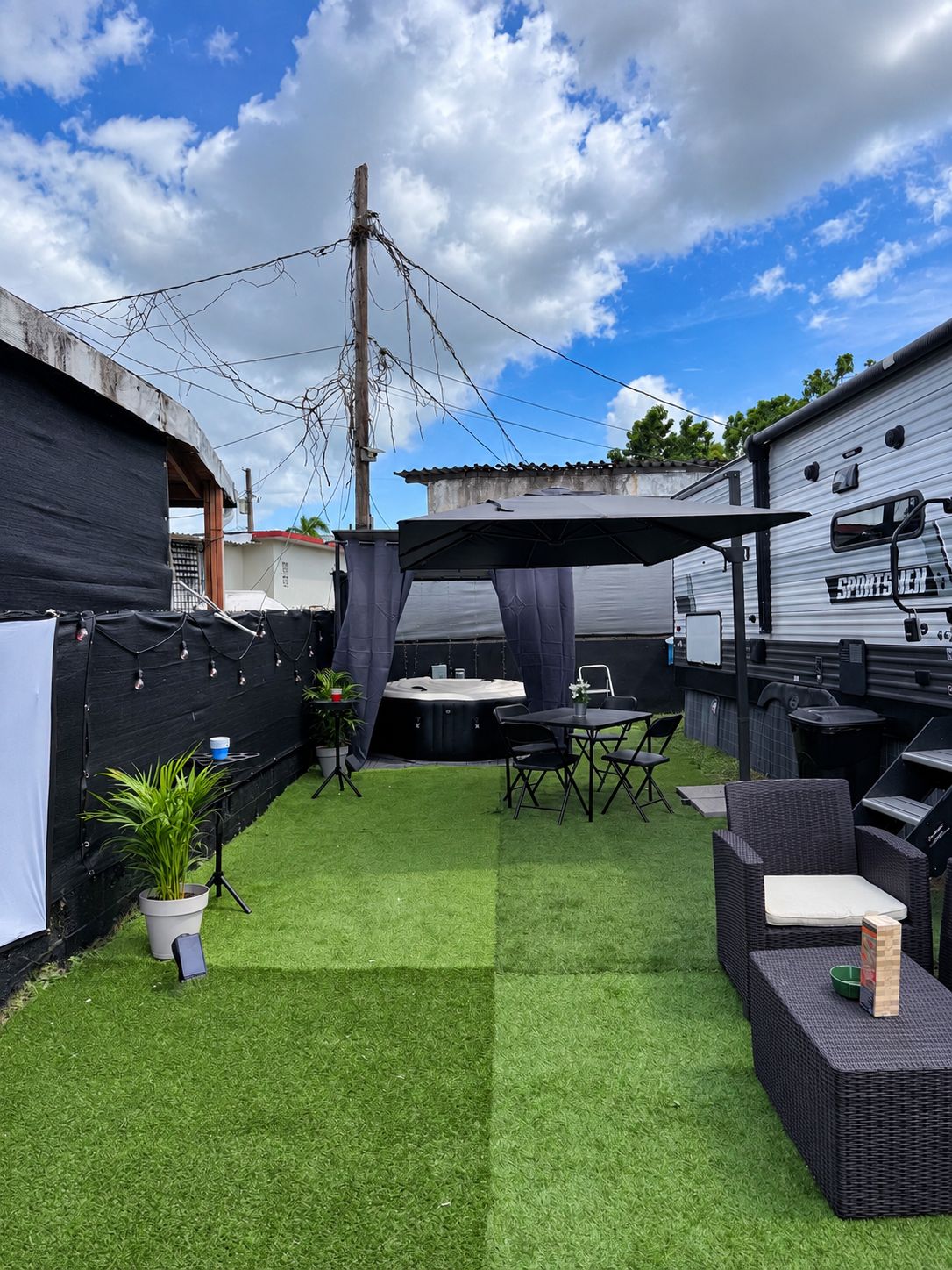 Un jardin avec une pelouse artificielle, un jacuzzi, du mobilier d’extérieur et un espace abrité équipé d’un barbecue.